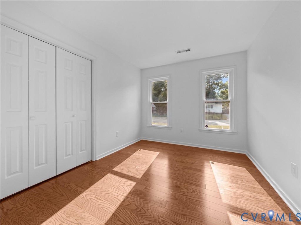 Wood-finish flooring, dual windows with white casing, and floor-to-ceiling bi-fold closet doors