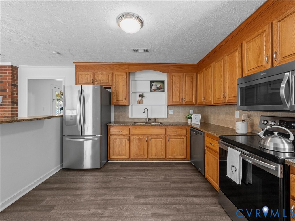 Kitchen featuring oak cabinetry, wood-finish flooring, stone-surfaced countertops, built-in stainless steel appliances, and a recessed wall niche
