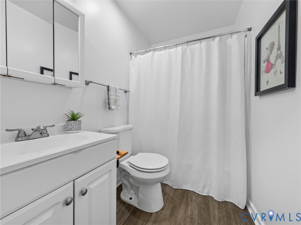 Bathroom featuring wood-finish flooring, a white vanity cabinet with an integrated sink, polished metal faucet, and a wall-mounted mirrored medicine cabinet