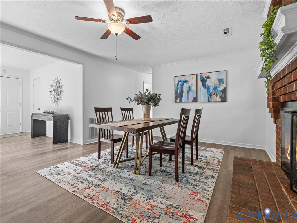 Wood-finish flooring, red brick fireplace with a white mantel, and ceiling fan with integrated lighting