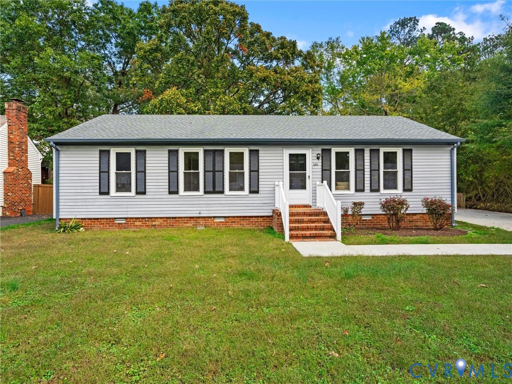 Ranch-style exterior featuring light-toned vinyl siding, dark shutters, a brick foundation, a central brick chimney, and a white-railed entrance Ranch-style exterior featuring light-toned vinyl siding, dark shutters, a brick foundation, a central brick chimney, and a white-railed entrance