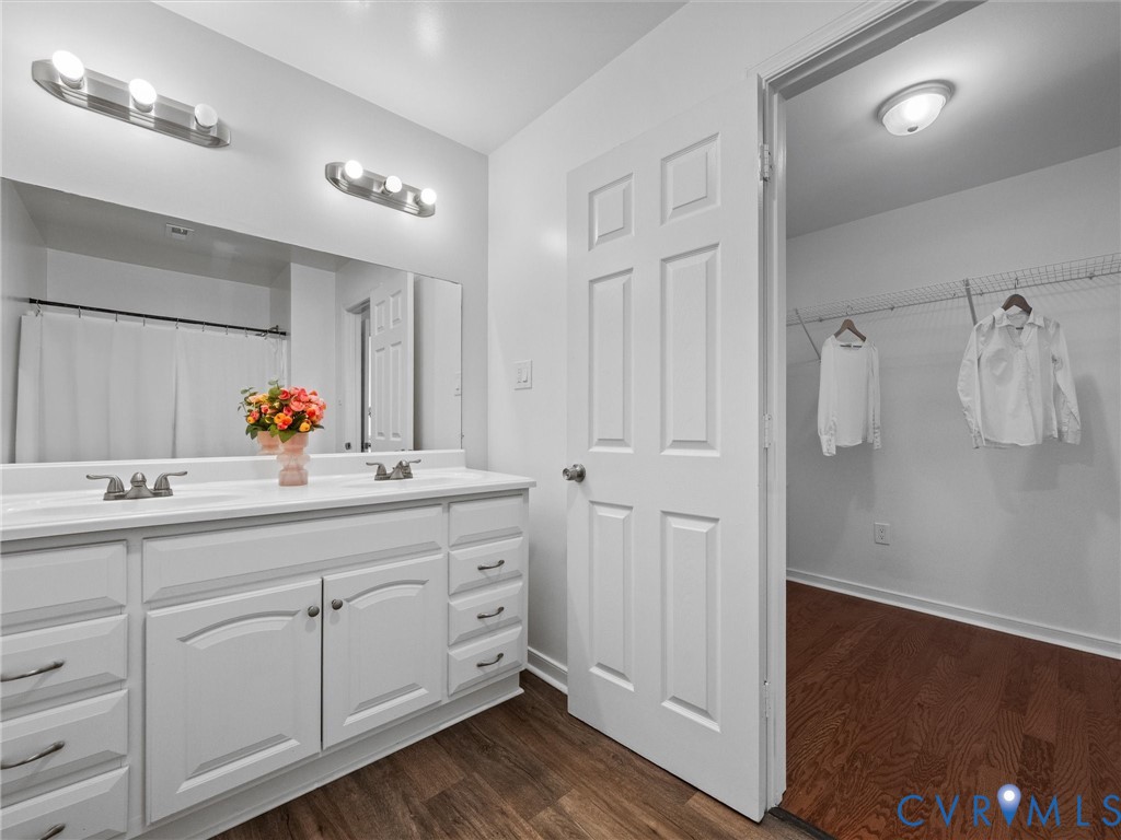 Dual-sink vanity with white cabinetry and expansive wall-mounted mirror, brushed-nickel lighting fixtures, six-panel interior door, and wood-finish flooring