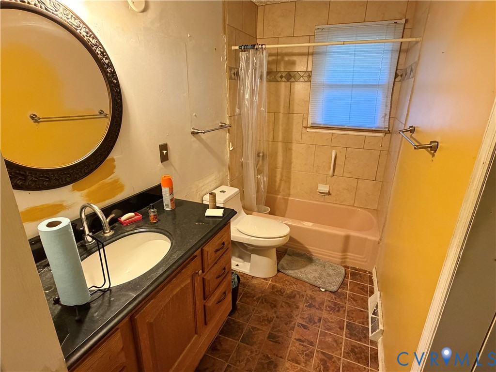 Bathroom featuring a wooden vanity with a dark countertop, integrated basin, tub and shower combination with tile surround, and tile flooring