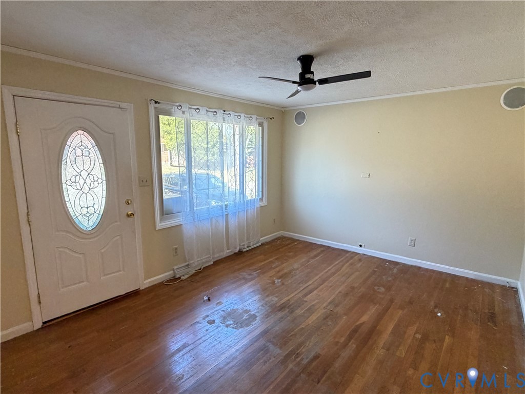 Wood-finish flooring, white exterior door with oval glass inset, large multi-pane window, and ceiling fan with integrated lighting