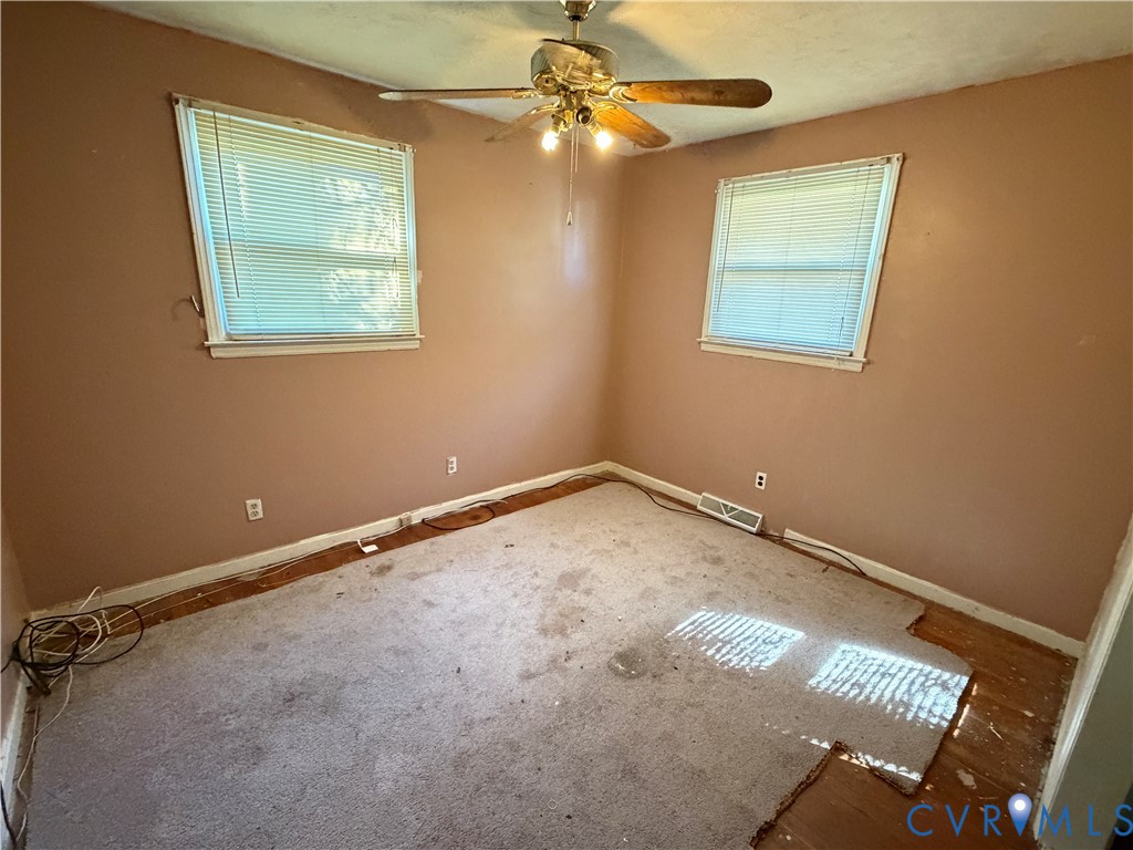 Room featuring two windows, neutral-toned walls, and a ceiling-mounted light fixture with a fan