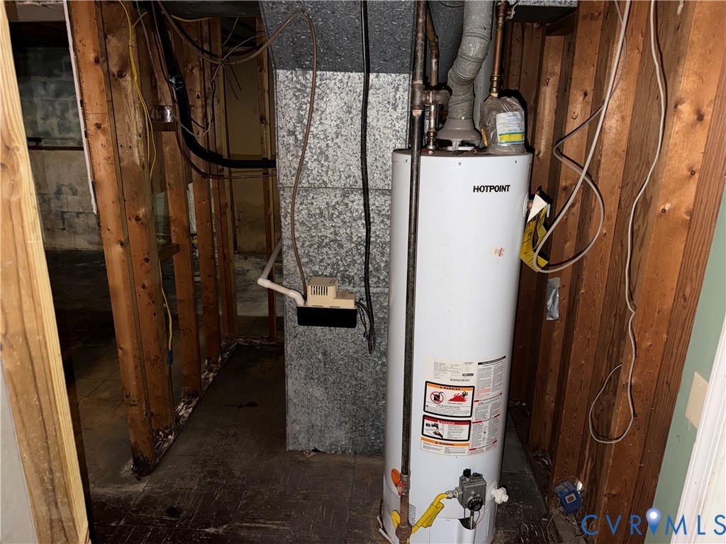 Hotpoint water heater featuring metal flue venting, installed alongside a masonry chimney stack and exposed wood framing