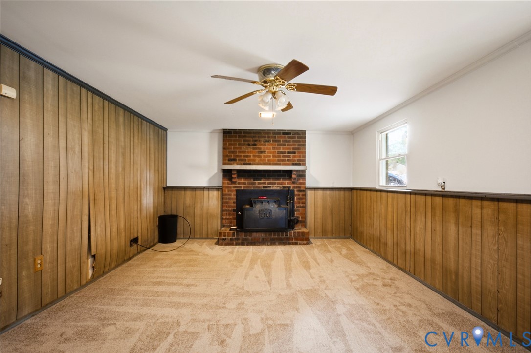 Floor-to-ceiling wood paneling, red brick fireplace, wood-burning stove insert, and a ceiling-mounted light fixture with a fan