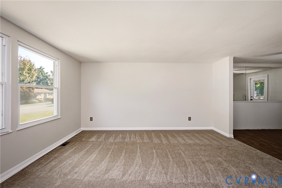 Neutral-toned interior space featuring light-colored wall paint, plush carpeting, double-hung windows, and a wide interior opening