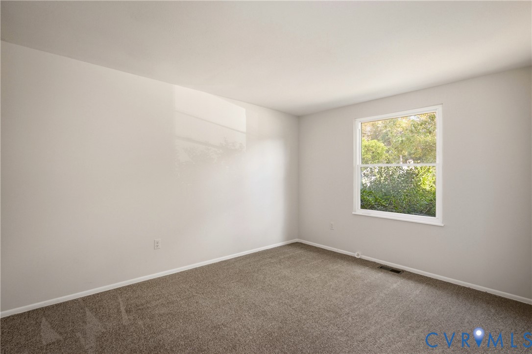 Neutral-toned interior featuring wall-to-wall carpeting and a single-pane window with external foliage