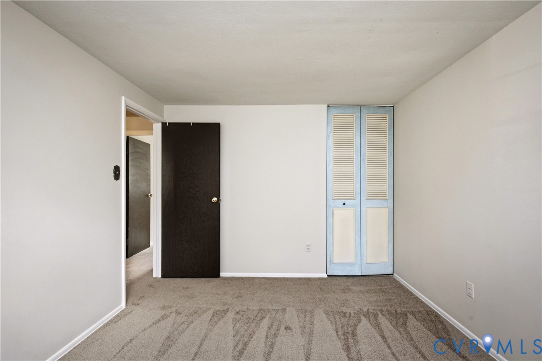 Interior space featuring neutral wall tones, carpeted flooring, a solid-core interior door, and a bi-fold closet door with louvered accents