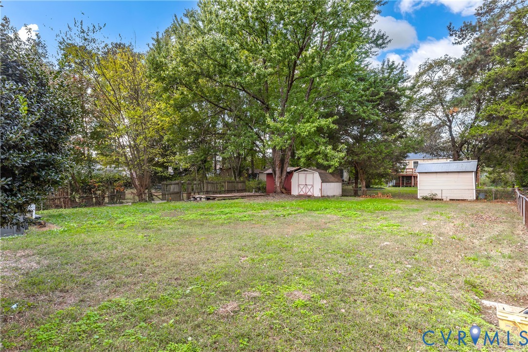 Expansive backyard featuring mature trees, wood fencing, and two detached storage structures