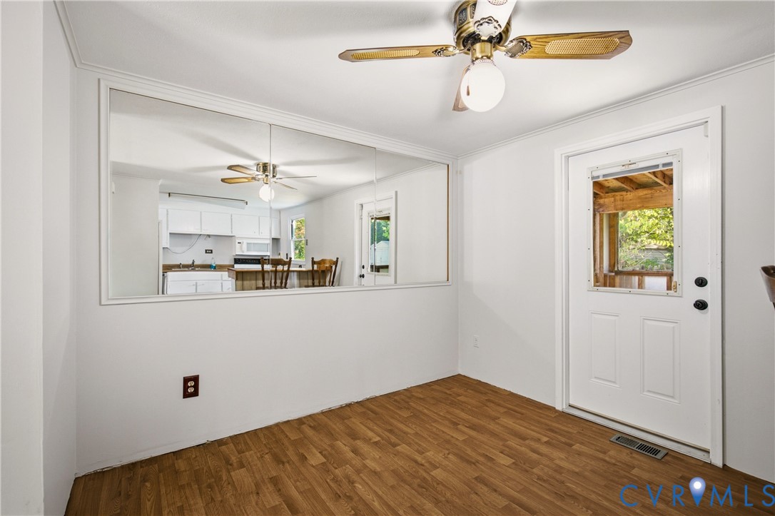 Wood-finish flooring, white wall-mounted mirror, ceiling fan with integrated lighting, and exterior entry door with windowed inset