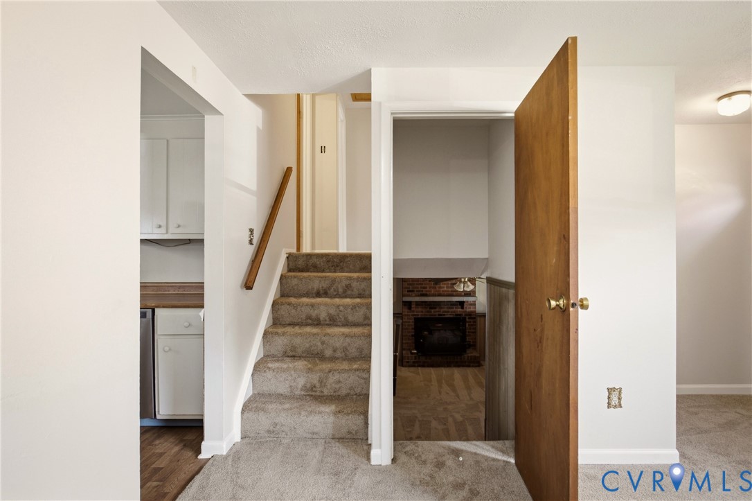 Interior space featuring carpeted staircase with wood handrail, brick-surround fireplace, flush-mount ceiling lighting, and solid-core wood door