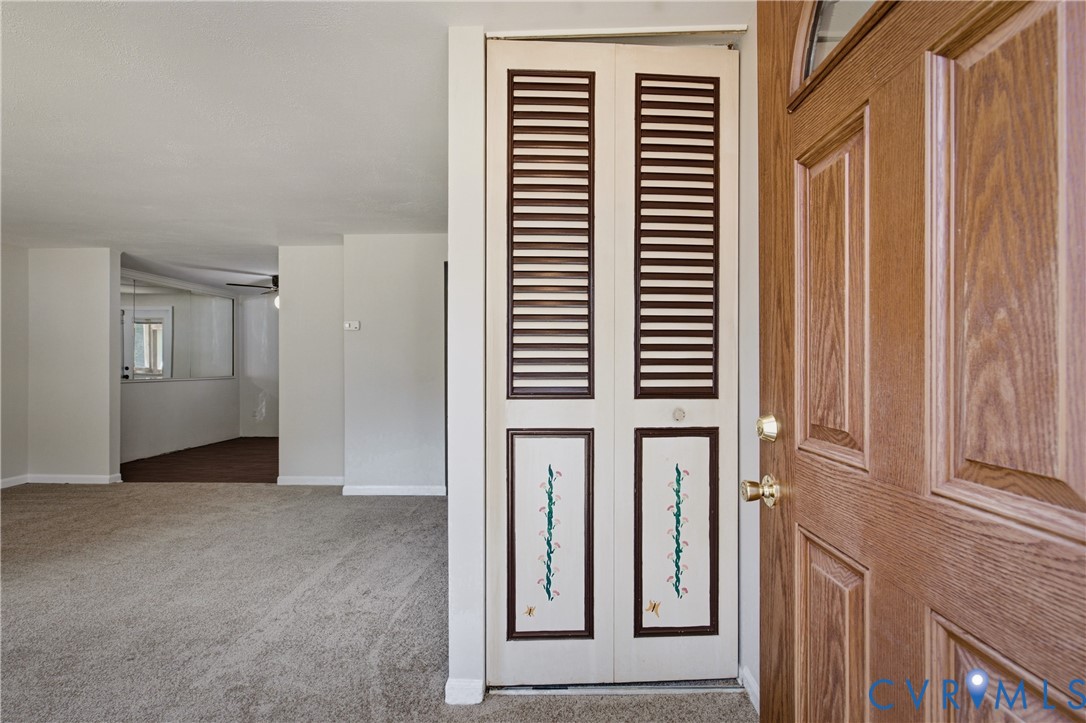 Entryway featuring a wood-finish front door with a half-moon light, bi-fold closet doors with louvered panels, and wall-to-wall carpeting