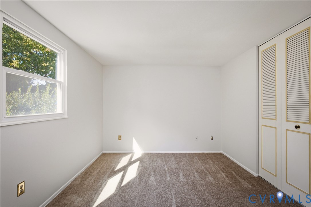Neutral interior featuring wall-to-wall carpeting, a multi-pane window, and built-in closet storage with louvered doors