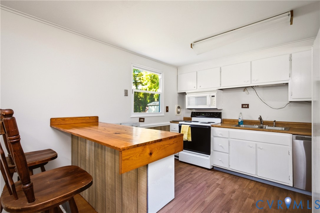 Kitchen featuring white cabinetry, wood-finish flooring, a wood-topped built-in breakfast bar, and a double-basin stainless steel sink