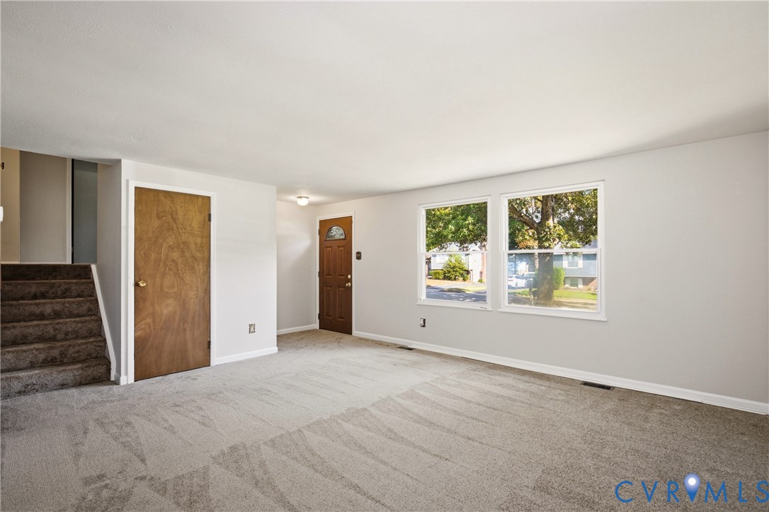 Neutral interior space featuring wall-to-wall carpeting, dual-pane windows, a wood-finish interior door, and a staircase with carpeted treads
