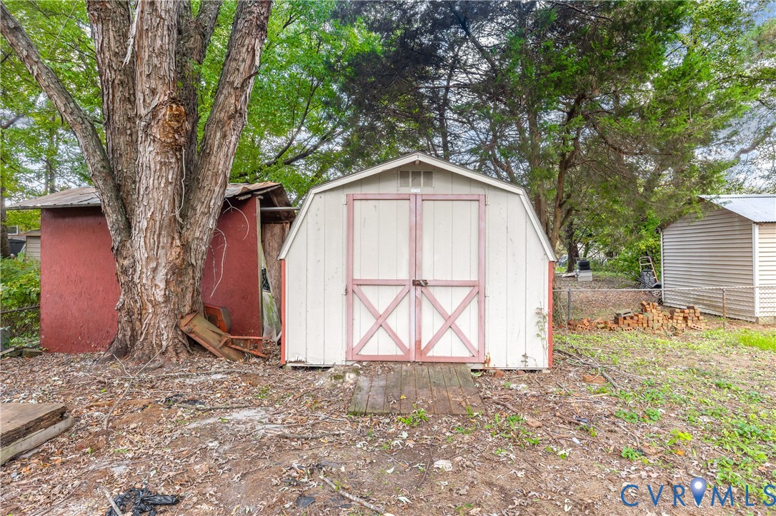 Barn-style storage shed featuring double doors and a wood-plank threshold, positioned on a lot with mature trees