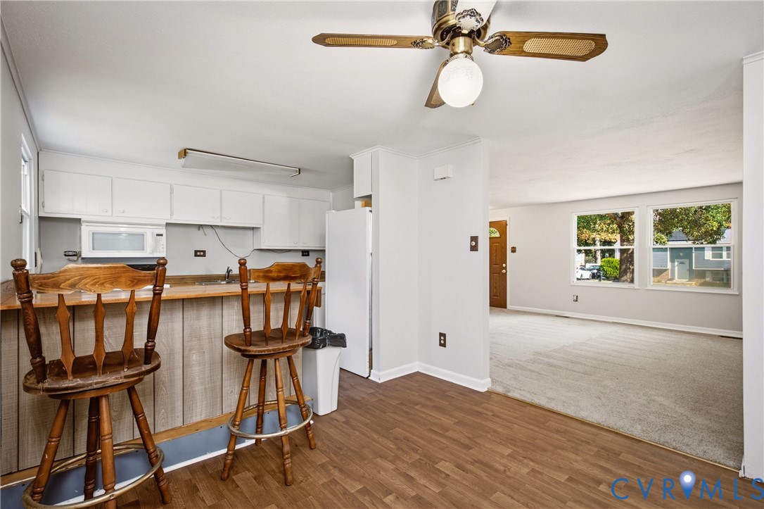 Kitchen featuring white cabinetry, a built-in microwave, wood-finish flooring, and a breakfast bar with wood paneling, complemented by a ceiling fan with integrated lighting