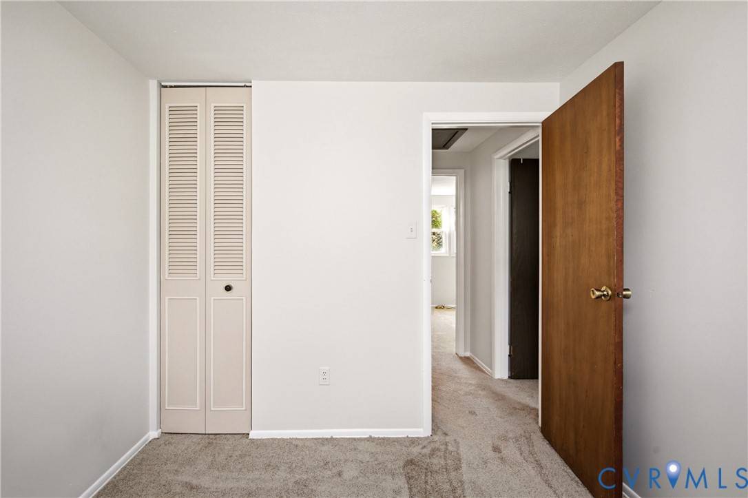 Neutral interior featuring light-toned wall paint, neutral carpeting, and a bi-fold louvered closet door with a natural wood-finish interior door