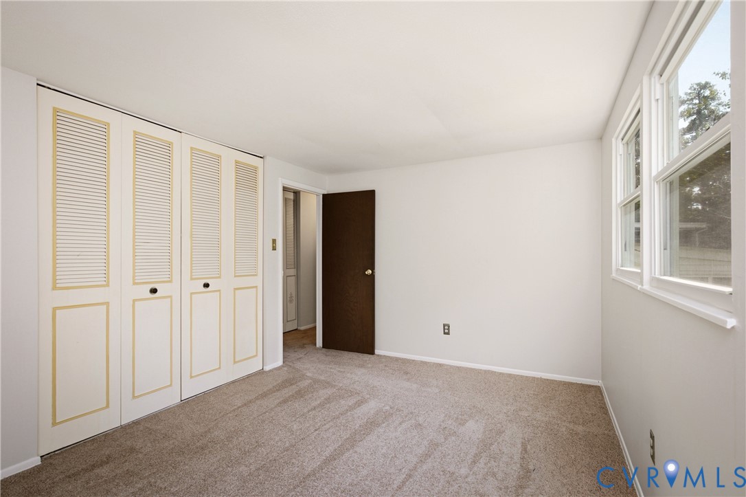 Neutral-toned carpeted flooring, wall-to-wall closet featuring white louvered doors, double-pane windows with white trim, and a dark wood interior door