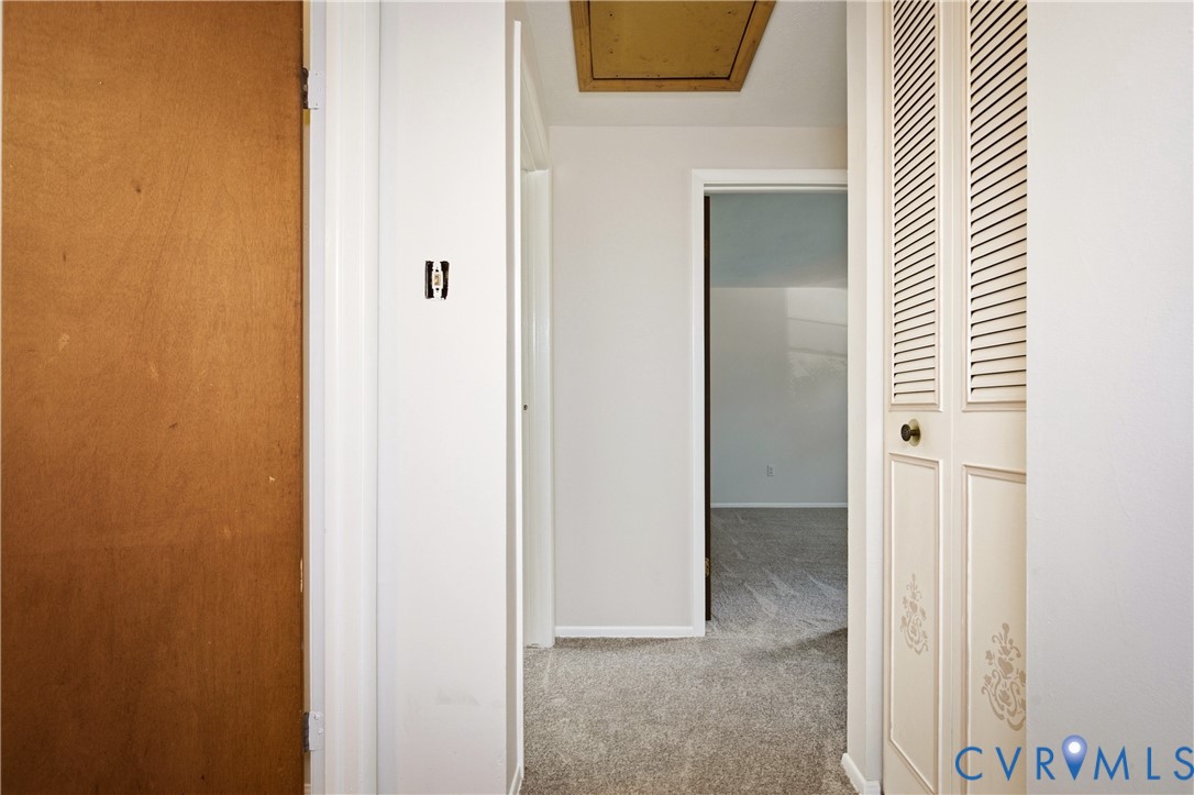Hallway featuring interior louvered bi-fold closet doors, a solid wood-finish door, and ceiling access panel