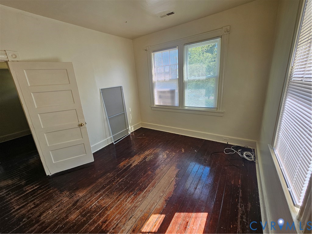 Interior room featuring dark-stained hardwood flooring, multi-pane windows with trim casing, and a five-panel interior door Interior room featuring dark-stained hardwood flooring, multi-pane windows with trim casing, and a five-panel interior door