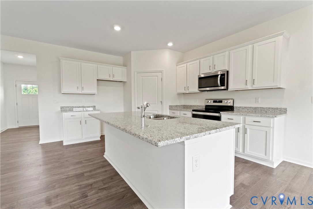 Modern kitchen featuring a central island with an undermount sink, granite-style countertops, white cabinetry, stainless steel appliances, and wood-finish flooring
