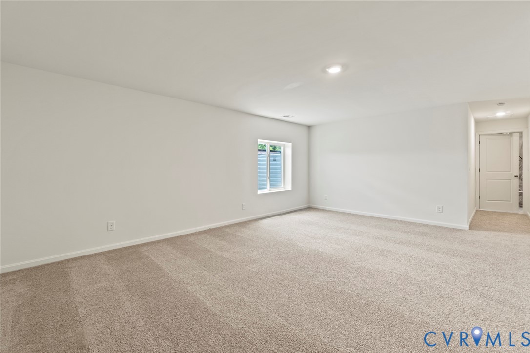 Spacious room featuring neutral carpet flooring, white painted walls, a window with a window well, and recessed lighting