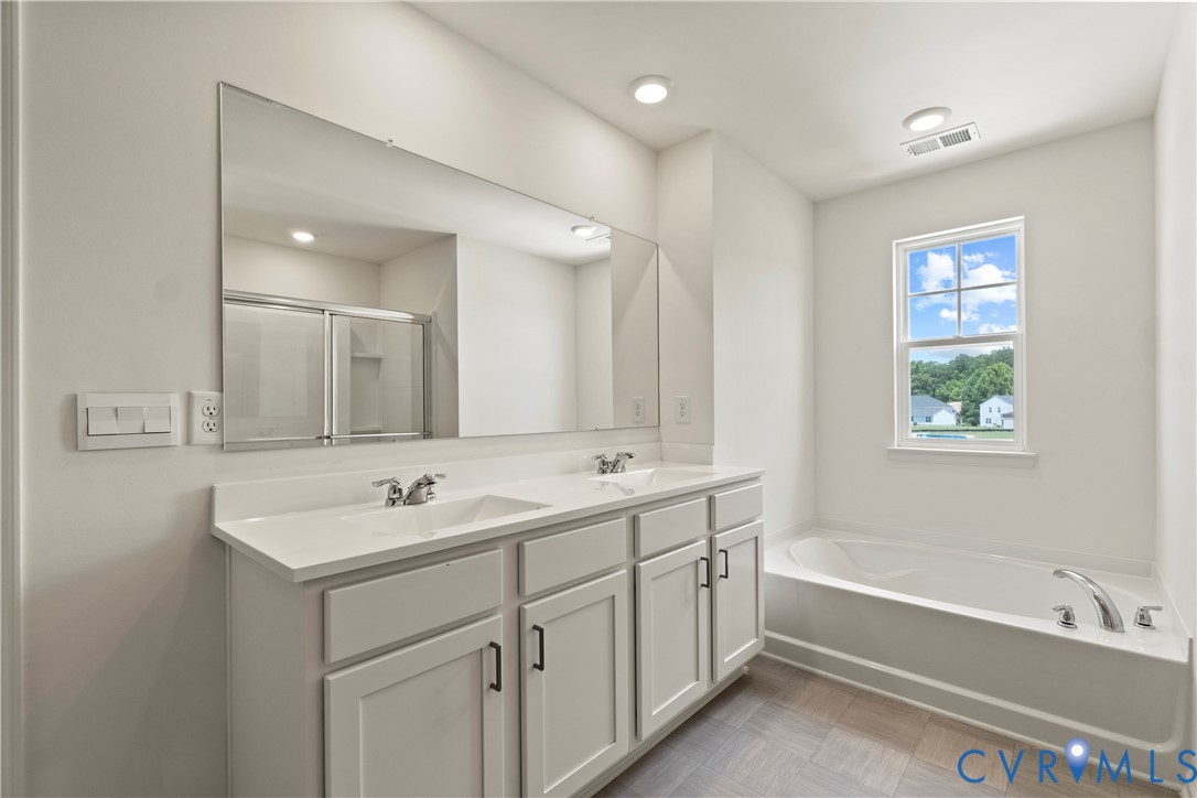 Bathroom featuring a dual vanity with white cabinetry and integrated sinks, a large wall-mounted mirror, a built-in bathtub with chrome fixtures, and a shower enclosure with sliding glass doors