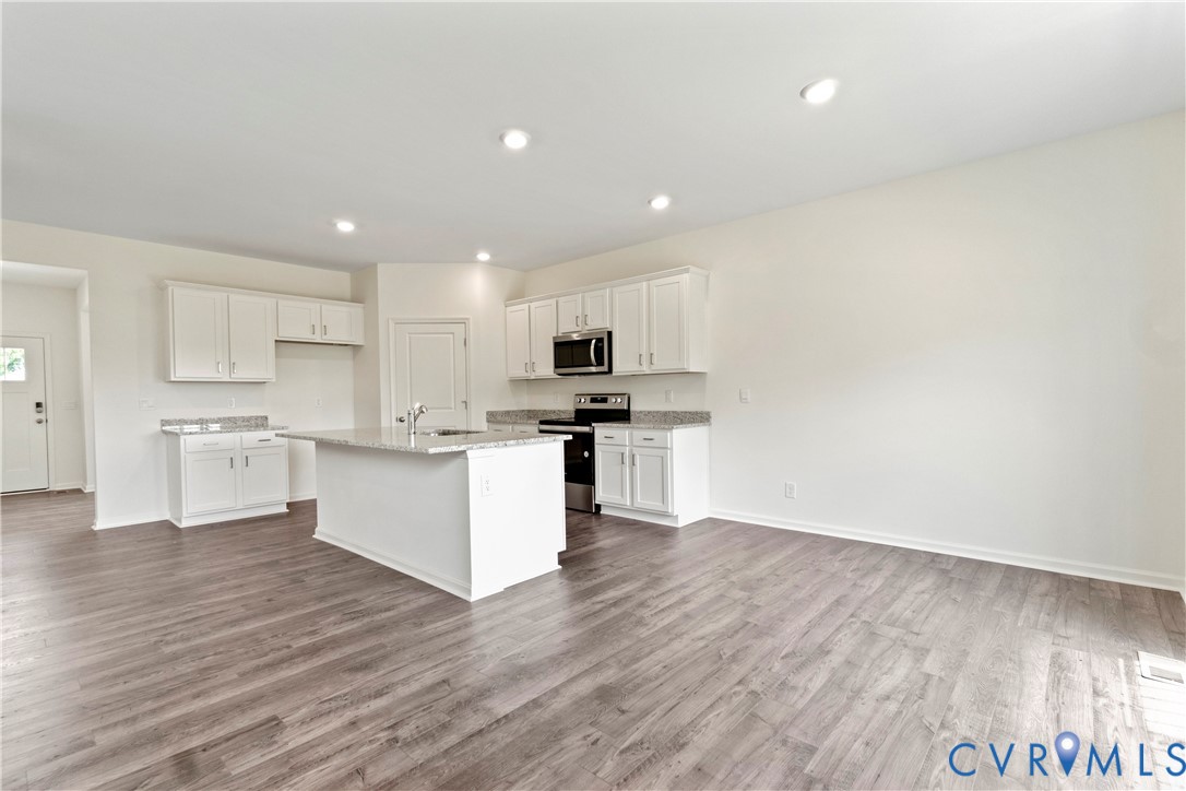 Open-concept kitchen featuring an island with a stainless steel sink, light-toned cabinetry, granite countertops, and wood-finish flooring