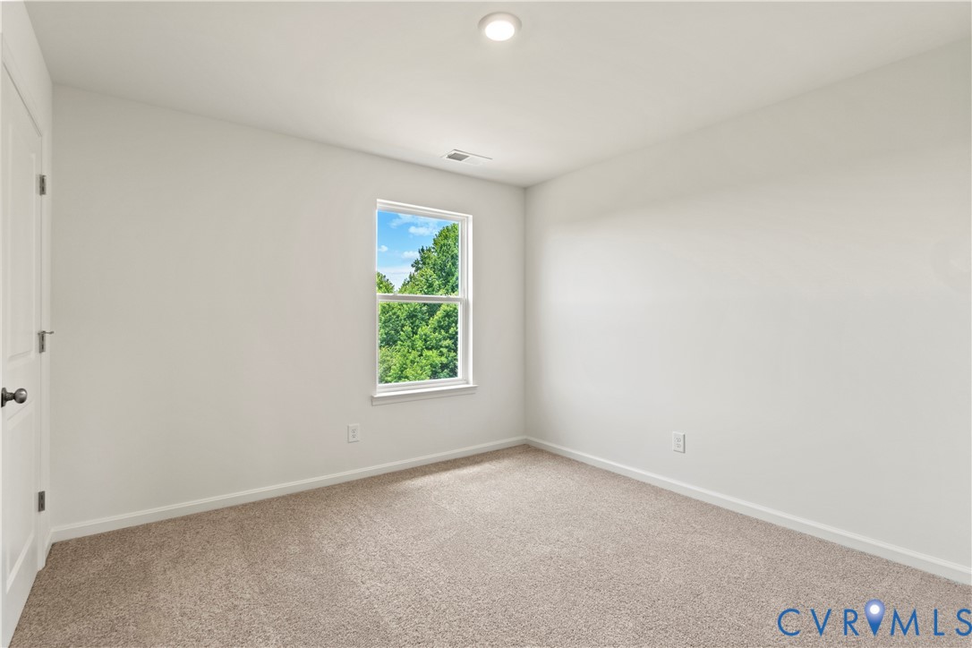 Bright interior space featuring neutral wall tones, carpet flooring, a window with a green tree backdrop, a recessed ceiling light, and a white paneled door
