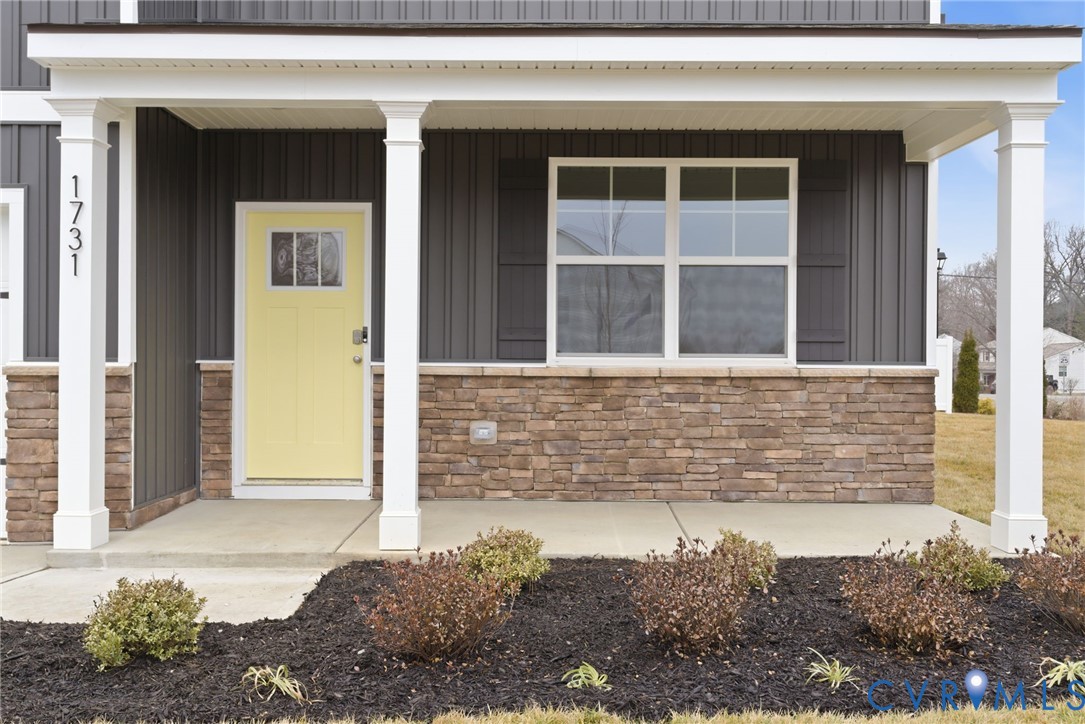Inviting front porch featuring a vibrant yellow door with transom window detail, white architectural columns, dark vertical siding, and a stacked stone foundation