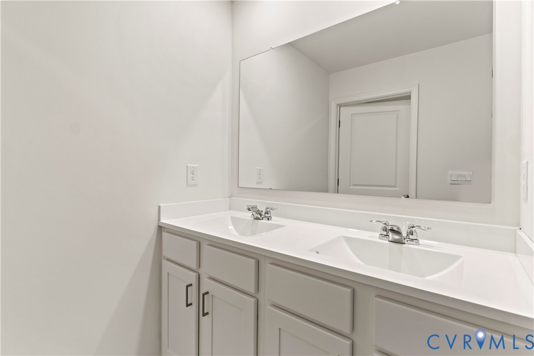 Double vanity featuring white cabinetry with shaker-style doors and dark hardware, integrated sinks, white countertops, and chrome faucets