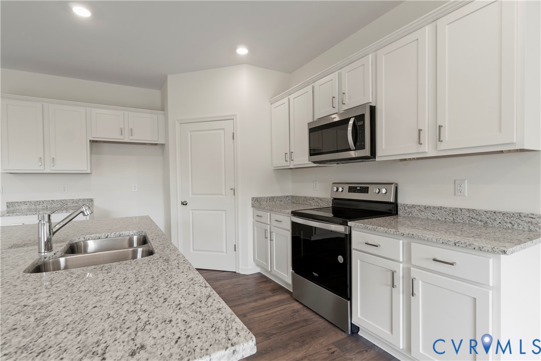 Kitchen featuring a double basin stainless steel sink, chrome faucet, white cabinetry, granite countertops, and stainless steel appliances