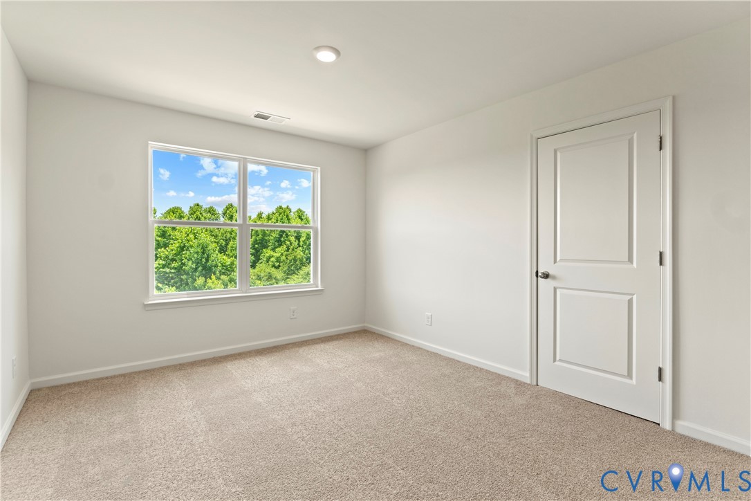 Spacious room featuring neutral carpeting, a large multipane window, and a two-panel door with brushed nickel hardware