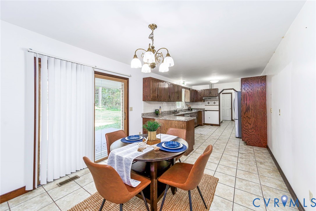 Kitchen featuring wood cabinetry, stone-finish countertops, ceramic tile flooring, a multi-bulb chandelier, and a sliding glass door