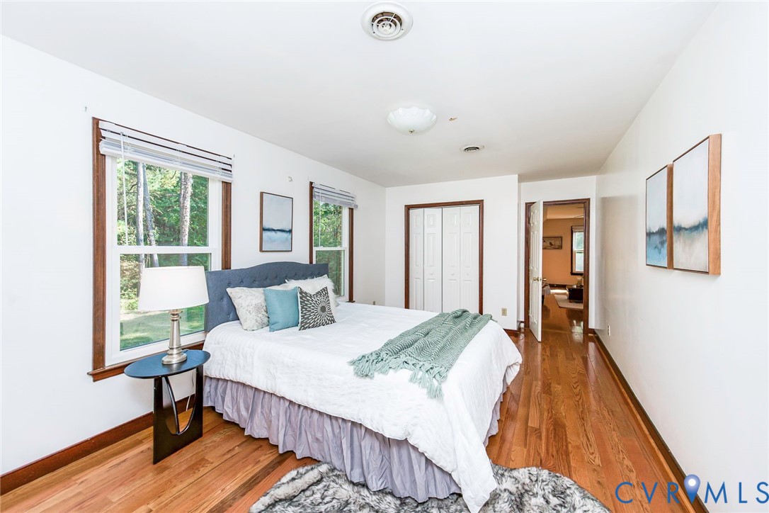 Bedroom featuring wood-finish flooring, dual windows with wood trim, and bi-fold closet doors