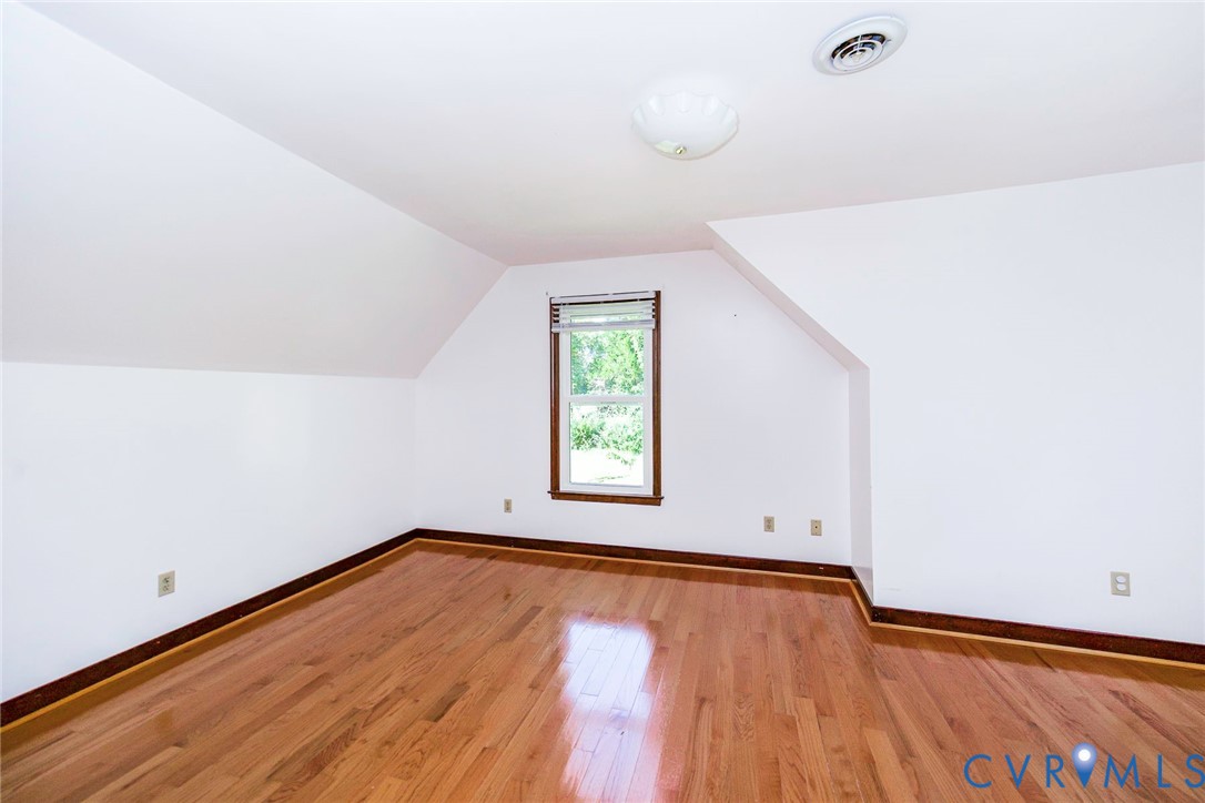 Interior space featuring wood-finish flooring, a double-hung window with dark trim, sloped ceilings, and a flush-mount light fixture