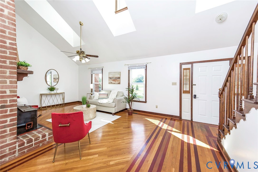 Vaulted ceiling with skylights, exposed brick fireplace, inlaid wood-finish flooring, and open staircase with wooden banister Vaulted ceiling with skylights, exposed brick fireplace, inlaid wood-finish flooring, and open staircase with wooden banister
