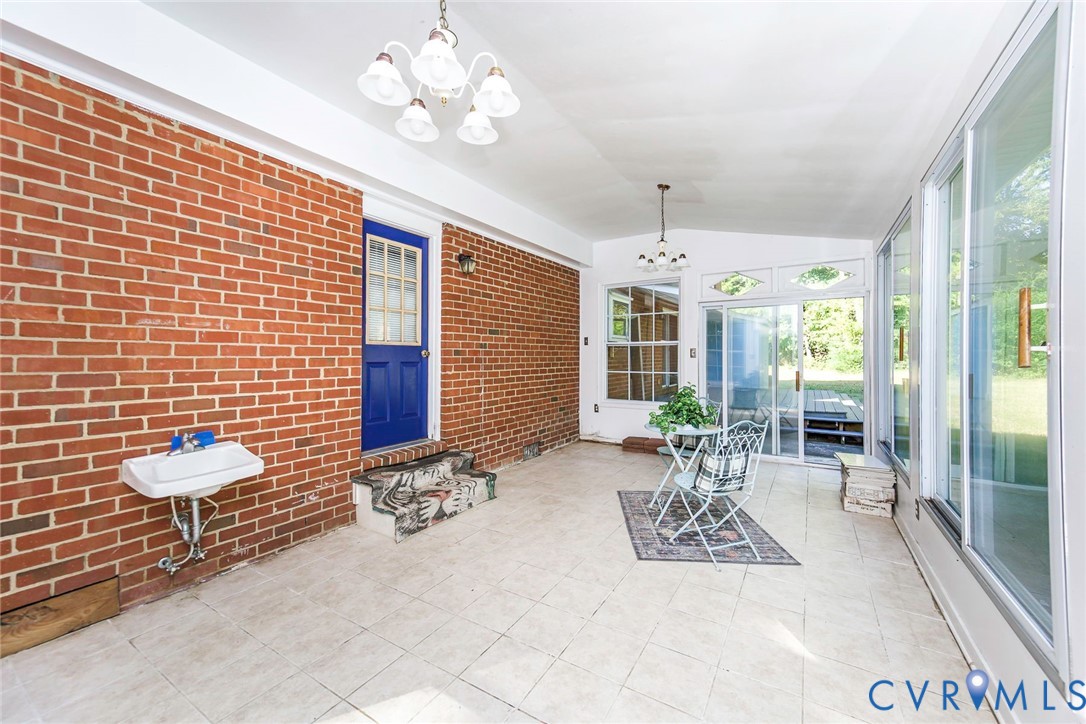 Enclosed sunroom featuring exposed brick walls, tile flooring, large sliding glass doors, and two multi-arm light fixtures