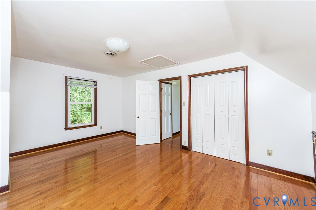 Wood-finish flooring, white paneled interior doors, bifold closet doors, and multi-pane window with wood-finish trim