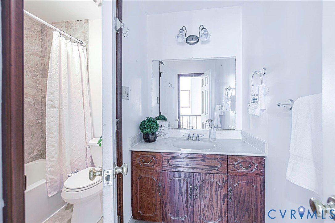 Bathroom featuring a wood vanity with a solid-surface countertop, an integrated oval sink, a wall-mounted mirror, and a tub-shower combination with tile-surround walls