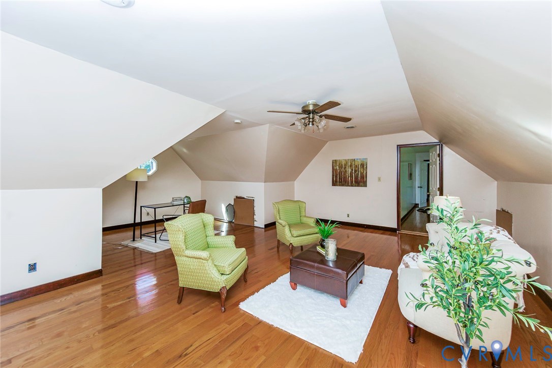 Spacious room featuring wood-finish flooring, vaulted ceilings with angled architectural lines, and a ceiling-mounted light fixture