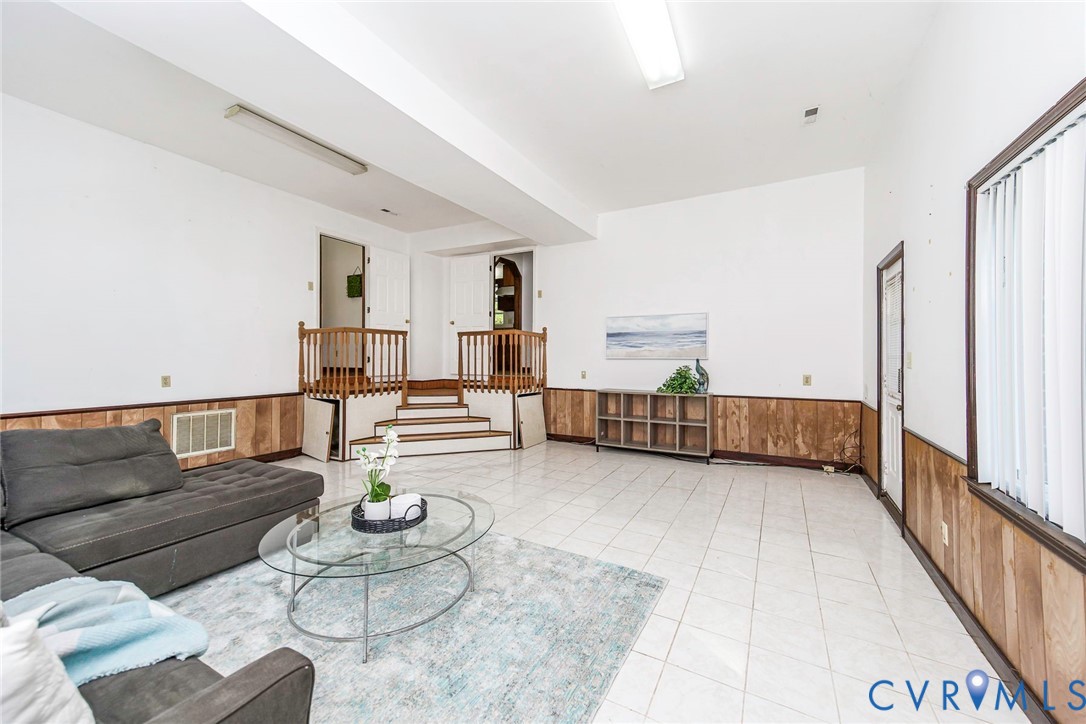 Spacious interior featuring light-colored tile flooring, wood panel wainscoting, and a multi-level staircase with wooden railing