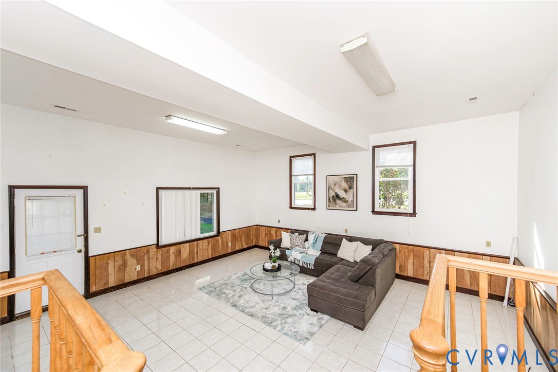 Interior space featuring ceramic tile flooring, wood-panel wainscoting, three windows, and a wood railing