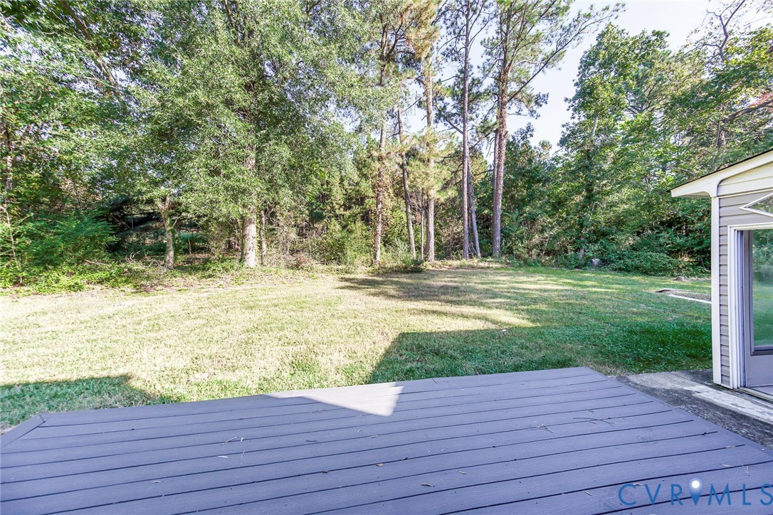 Rear exterior featuring a wood-finish deck, level lawn, and mature perimeter trees