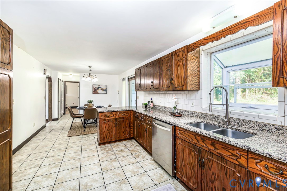 Kitchen featuring stained wood cabinetry, stone-finish countertops, subway tile backsplash, stainless steel dishwasher, and a garden window above a dual-basin sink Kitchen featuring stained wood cabinetry, stone-finish countertops, subway tile backsplash, stainless steel dishwasher, and a garden window above a dual-basin sink