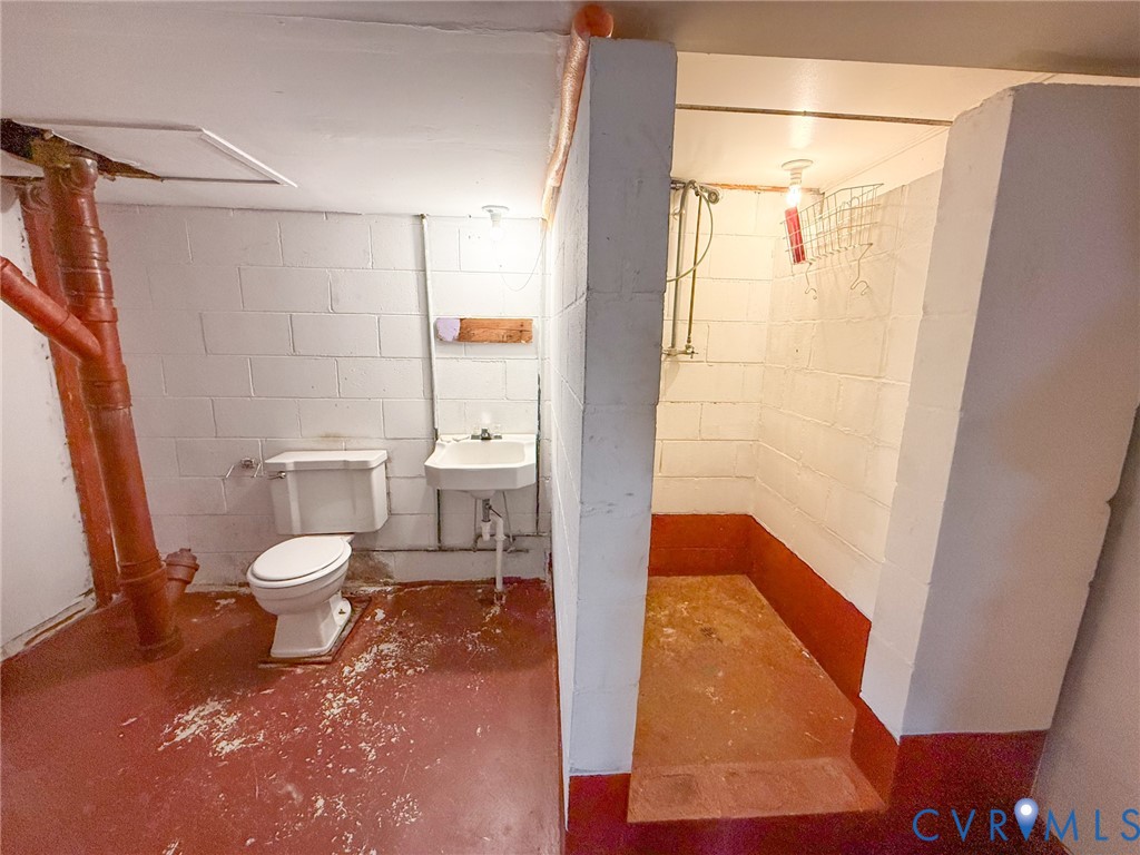 Utility area featuring concrete block walls, a pedestal sink, porcelain toilet, and a tiled shower stall
