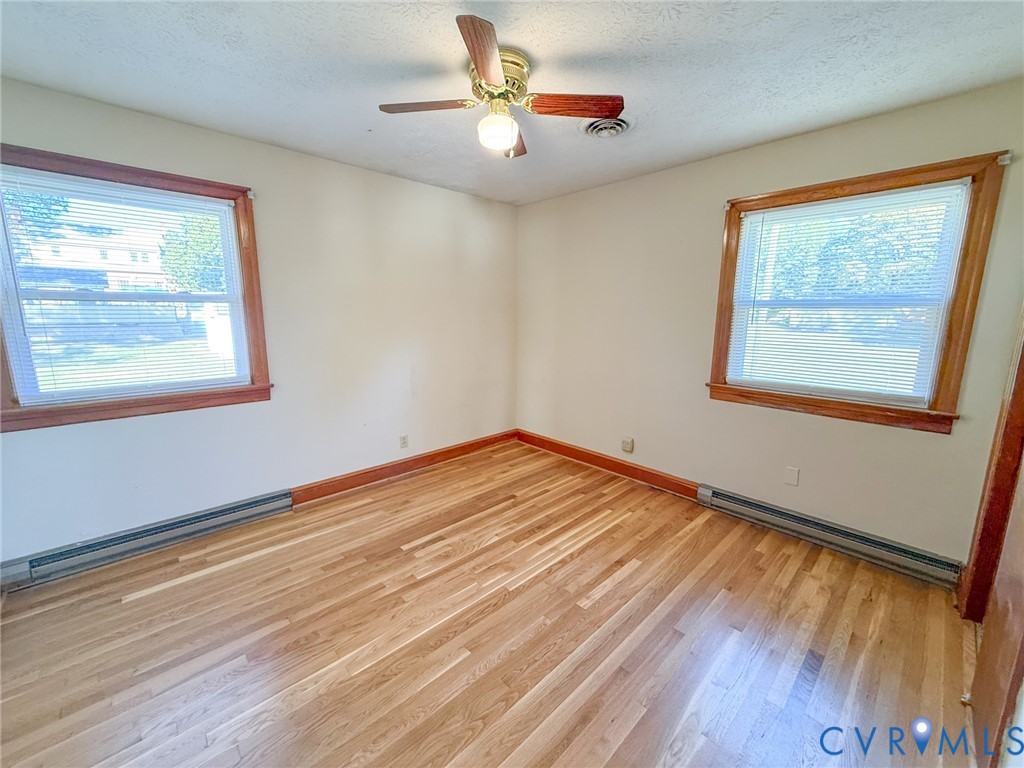 Wood-finish flooring, dual windows with wood trim, and a ceiling-mounted fan with light fixture